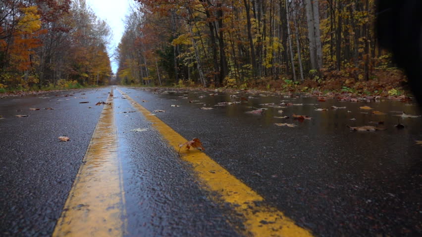 SLOW MOTION CLOSEUP: Black SUV car driving along an empty forest road, over fallen autumn tree leaves in reainy fall. Black jeep car driving fast along the wet slippery road, swirling colorful leaves