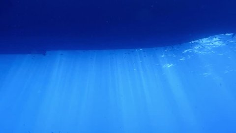 Underwater sun rays under the hull of the ship. Scuba diving in the blue exotic sea. Safari ship for adventure trips and sun rays.