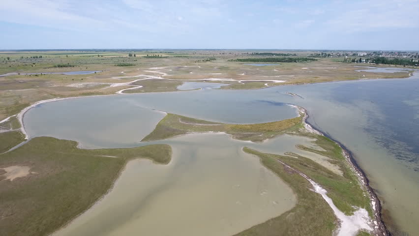 The Black Sea shelf with curvy, thin and long islands is covered with green wetland and sand. The weed is seen in the transparent blue waters on a sunny day in summer