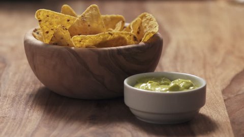 Slow motion young female hand dipping nachos in guacamole sauce