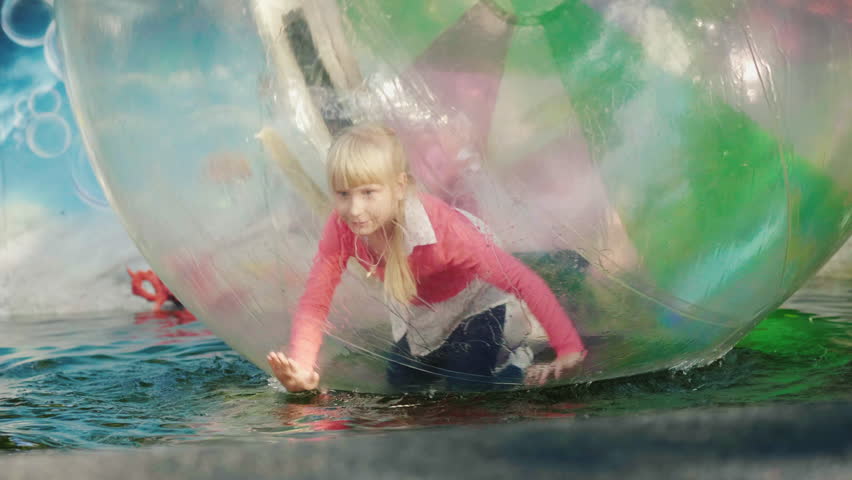 The child plays inside a transparent ball on the water. Recreation in amusement park, happy holidays