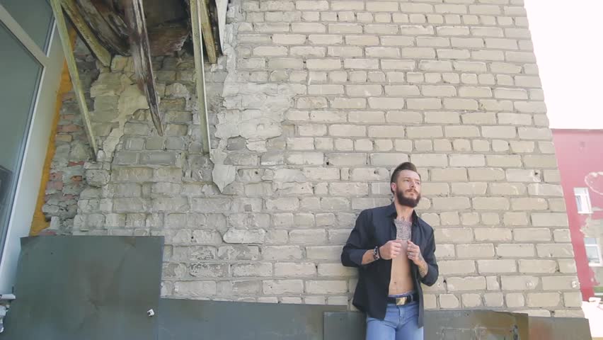 a handsome brutal man with a beard in jeans and a black T-shirt on the background of a gray brick wall