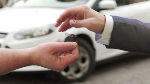 A car being bought / sold. A man buying / selling  a car to another man and handing over the key.