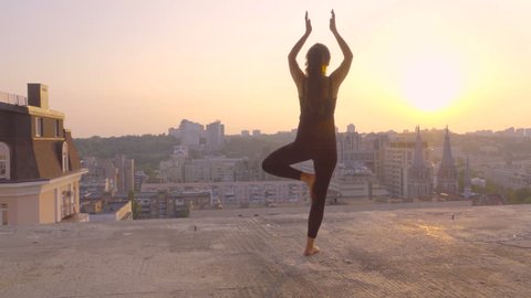 Sporty brunette doing yoga exercise on the rooftop at sunset