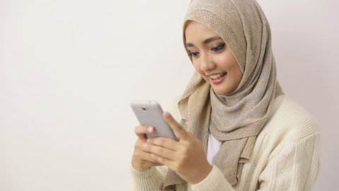 Portrait of a smiling beautiful muslim woman texting with her smartphone while sitting on a couch at home