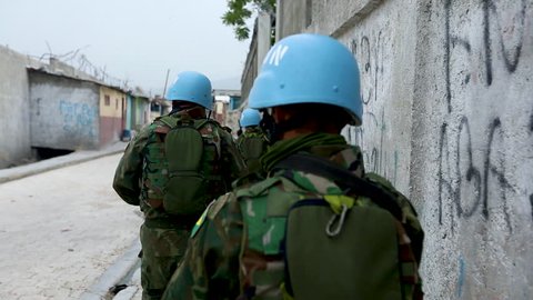 Close up following UN peacekeepers walking closesly to a wall down an empty street