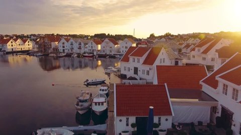 Flight over amazing city of Norway with beautiful harbor and city infrastructure at sunset. Top view of cozy port city Skudeneshavn, Norway. Beautiful white yachts and boats stand in the sea harbor.