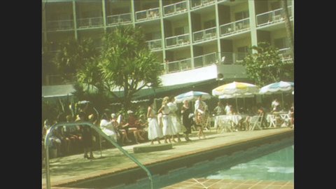 1940s: Women model clothing around pool at hotel. Woman lays on towel at the beach. Children play in ocean at the beach.