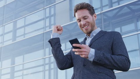 Success and achievement - happy businessman cheering celebrating looking at cell phone. Young urban professional successful business man receiving good news in business. Smartphone app concept