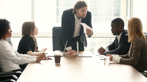 Angry boss scolding female employee for bad work result sitting at conference table, male director yelling at incompetent subordinate blaming for mistake in financial document at diverse team meeting