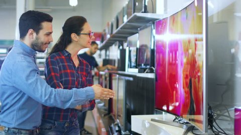 Young Couple Shopping for a New 4K UHD Television Set in the Electronics Store. They're Deciding on the Best Model for Their Happy Family House. Shot on RED EPIC-W 8K Helium Cinema Camera.