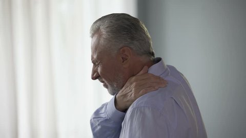 Aged man standing sideways, touching neck in acute pain, trying to move head