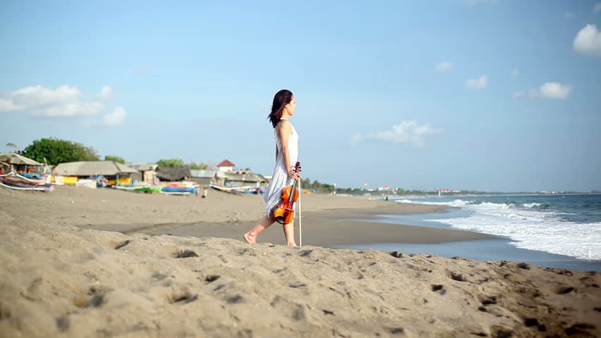 Young woman standing at coast and playing on violin