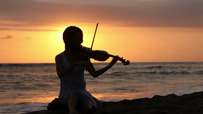 Silhouette of woman playing romantic music on violin on shore
