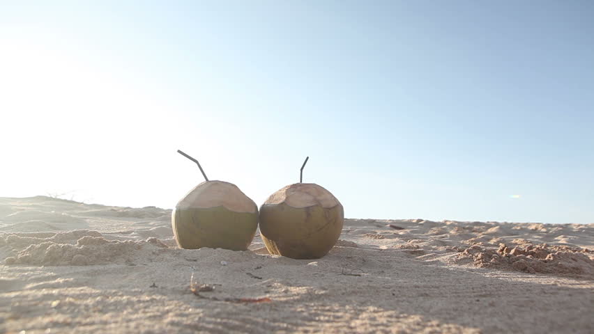 Two coconuts placed on sand and couple walking