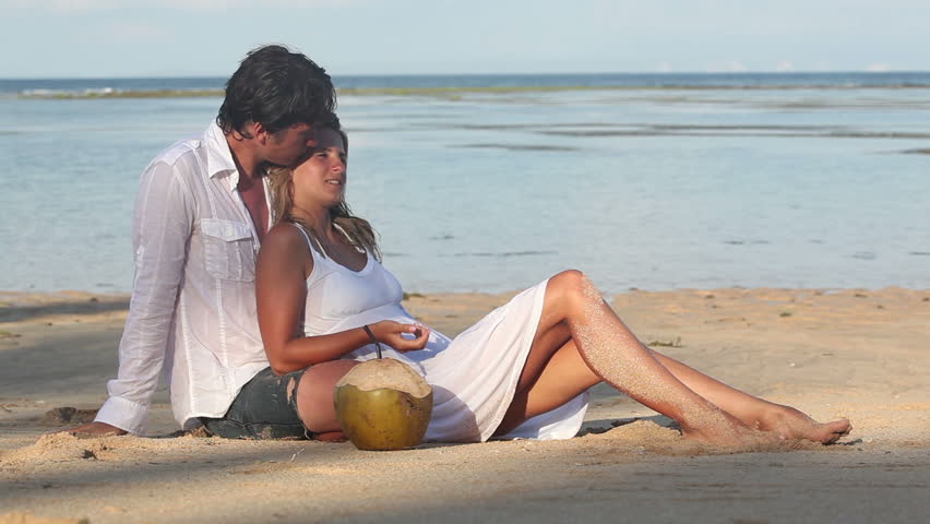 Attractive couple with coconuts sitting on beach