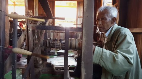 MYANMAR - CIRCA DECEMBER 2016 - Elderly Burmese man spins undyed lotus thread unto spool, Inle Lake, Myanmar