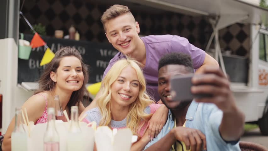 leisure and people concept - happy young friends taking selfie and showing peace hand sign at food truck