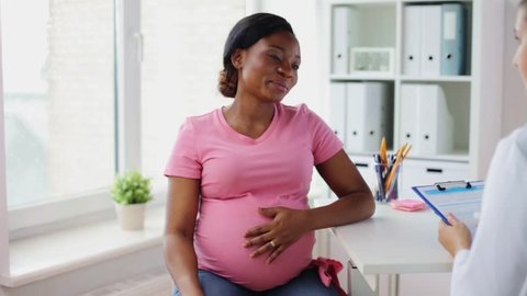 pregnancy, medicine, healthcare and people concept - gynecologist doctor with clipboard and happy pregnant african american woman talking at hospital