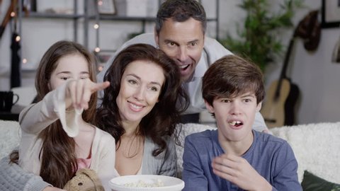 Happy caucasian family watching television and chatting as they eat popcorn together at home. In slow motion