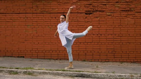 Modern ballet dancer. The young sporty woman dancing against the red brick wall in the street. 4K