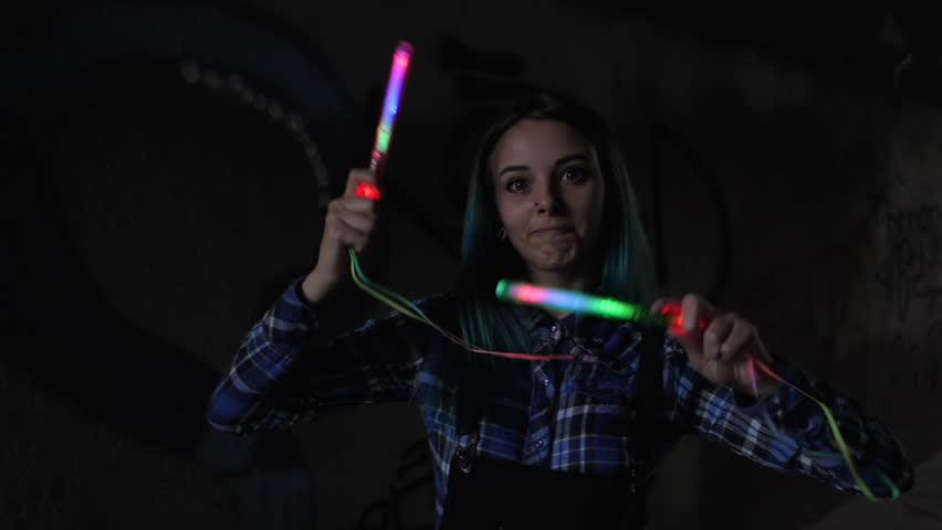 SLOW MOTION: Portrait of model girl with blue hair looks with colorful wand in hands. Close up. Beautiful young teenage in city tunnel having fun with magic flashing sticks