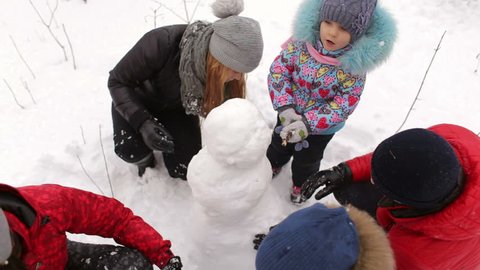 Young family with children building a snowman in the Park. Happy family playing with fresh snow in the woods.