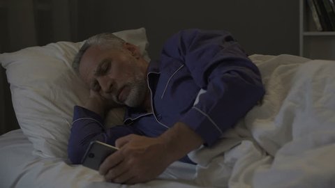 Addicted to smartphone senior man scrolling application instead of sleeping