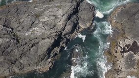 Aerial view looking down on the waves crushing onto the rocky Pacific Ocean Coast during a sunny summer day. Video taken near Tofino and Ucluelet in Vancouver Island, British Columbia, Canada.