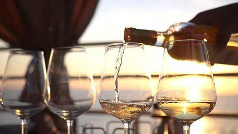 Pour white wine over clear glass glasses at sunset. HD, 1920x1080. slow motion