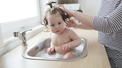 Baby taking bath in kitchen sink. sunny bathroom with window. Little girl bathing. Water fun for kids. Hygiene and skin care for children.