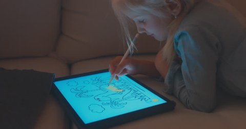 CU Cute Caucasian 5 y.o. girl coloring an image on digital tablet using stylus. Modern interior, evening shot. 4K UHD RAW edited footage