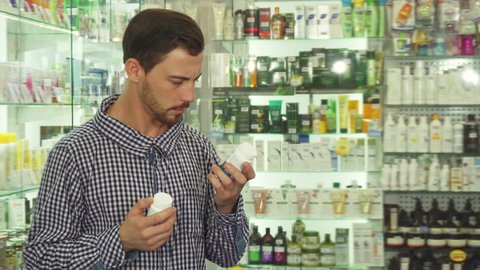 Man reading packaging of two drugs. He is hesitating which to choose. Patient is in drugstore
