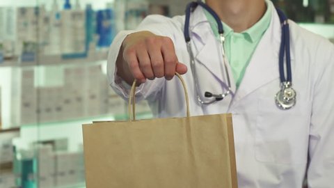 Doctor holding a package proposing it to camera. Accent on package, we only see his smile. Man is in drugstore