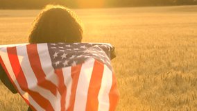 4K video clip of mixed race African American girl teenager female young woman holding an American USA Stars and Stripes flag in a wheat field at sunset or sunrise