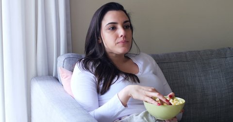 Beautiful woman eating popcorn on sofa at home 4k