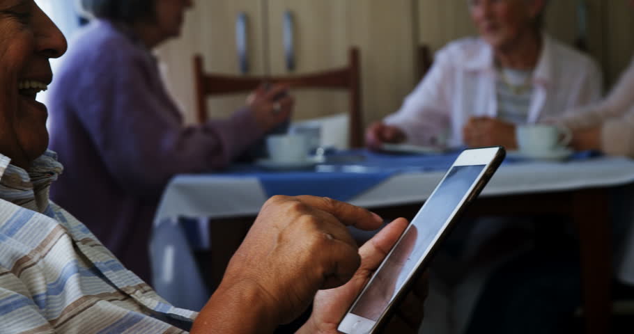 Senior Caucasian man using digital tablet with his friends sitting in background at retirement home 4k