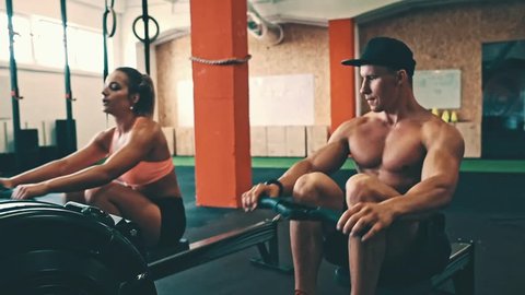 Athletic couple training on row ergometer machine at cross gym