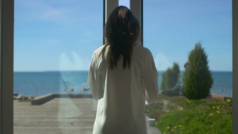 Following Shot of a Beautiful Brunette with Loose Hair Walking on the Sunny Terrace with Seaside View. It's Cloudless Morning and She's Really Happy. Shot on RED EPIC-W 8K Helium Cinema Camera.