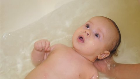 Baby bathes in bathtub with clear water and laughs. Slow motion.