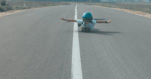 Little boy wearing helmet and styrofoam wings riding skateboard on a rural road, pretending to be a pilot. 4K UHD RAW edited footage