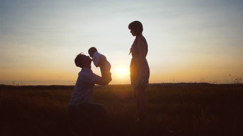 Mother gives baby to her father in arms against beautiful sunset, Slow motion