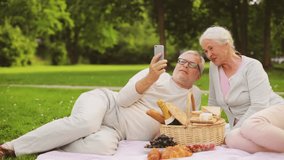 old age, leisure and people concept - happy senior couple with picnic basket and wine taking selfie by smartphone at summer park