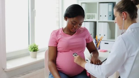 pregnancy, medicine, healthcare and people concept - gynecologist doctor with stethoscope listening to pregnant african american woman baby heartbeat at hospital