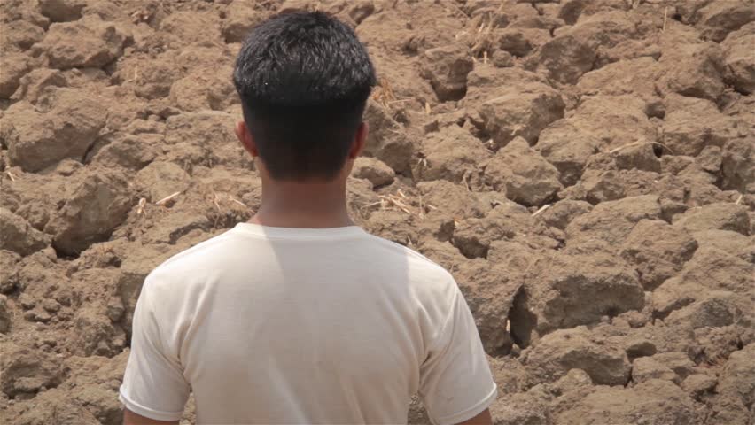 Devastated young Indian farmer standing against the dry and drought affected farmland, India