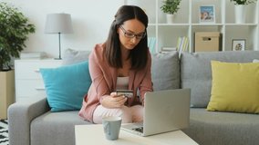 Young brunette woman in the glasses shopping online using laptop at home in the living room.