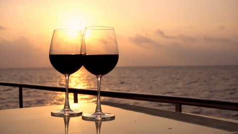 Romantic luxury evening on cruise yacht with winery setting. Glasses with red wine and tropical sunset with sea background, nobody