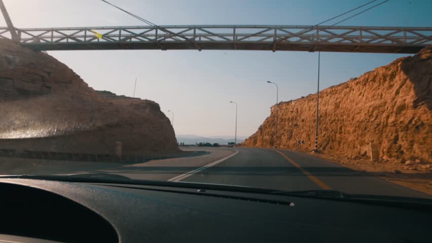 Driving a car on Red Rock Canyon Road in the Red Rock Canyon National Conservation Area in Nevada. The late afternoon sun creates a lens flare over the roadway.
