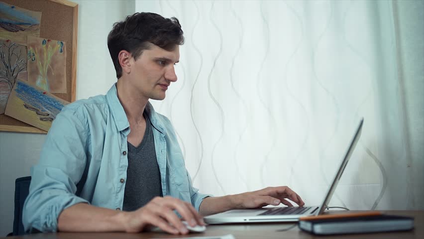 Casual dressed freelancer using laptop at office. Board with color sketches at wall behind Royalty-Free Stock Footage #30760723