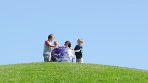 Group of children push a large ball down a hill.